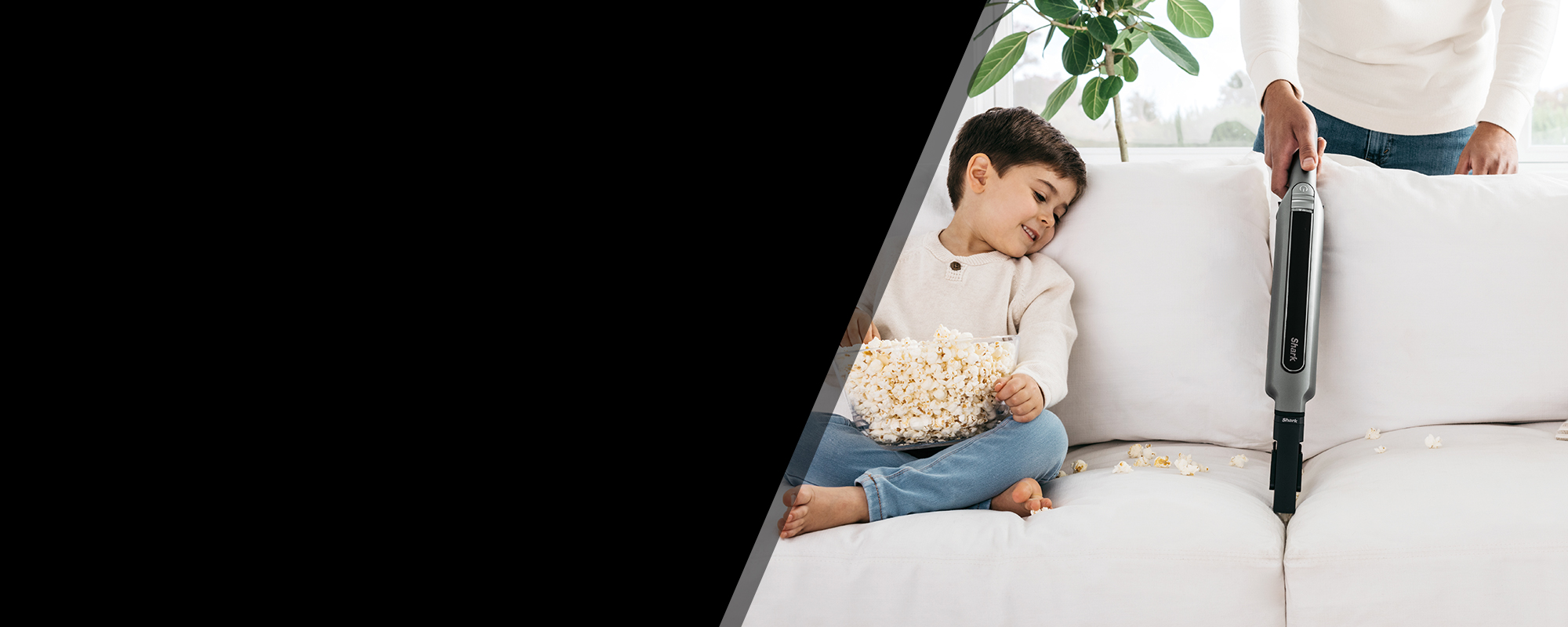 Shark handheld vacuuming split popcorn from couch next to child